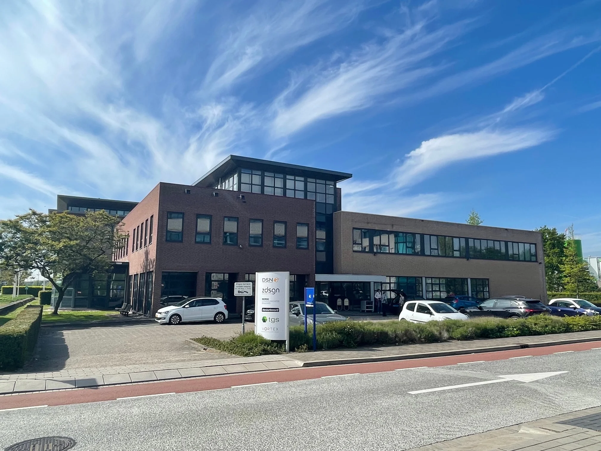 Kantoorgebouw aan de Rivium 4e Straat met geparkeerde auto's en een helderblauwe lucht.